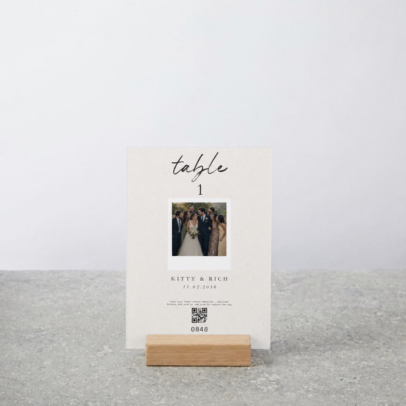 A Polajoy table card in its oak stand: the table number, the couple's photo as a retroprint, their names and date, and the scan-to-join code